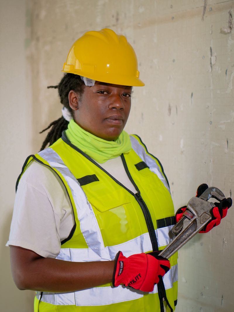 Licensed plumber in a high-visibility vest holding a pipe wrench